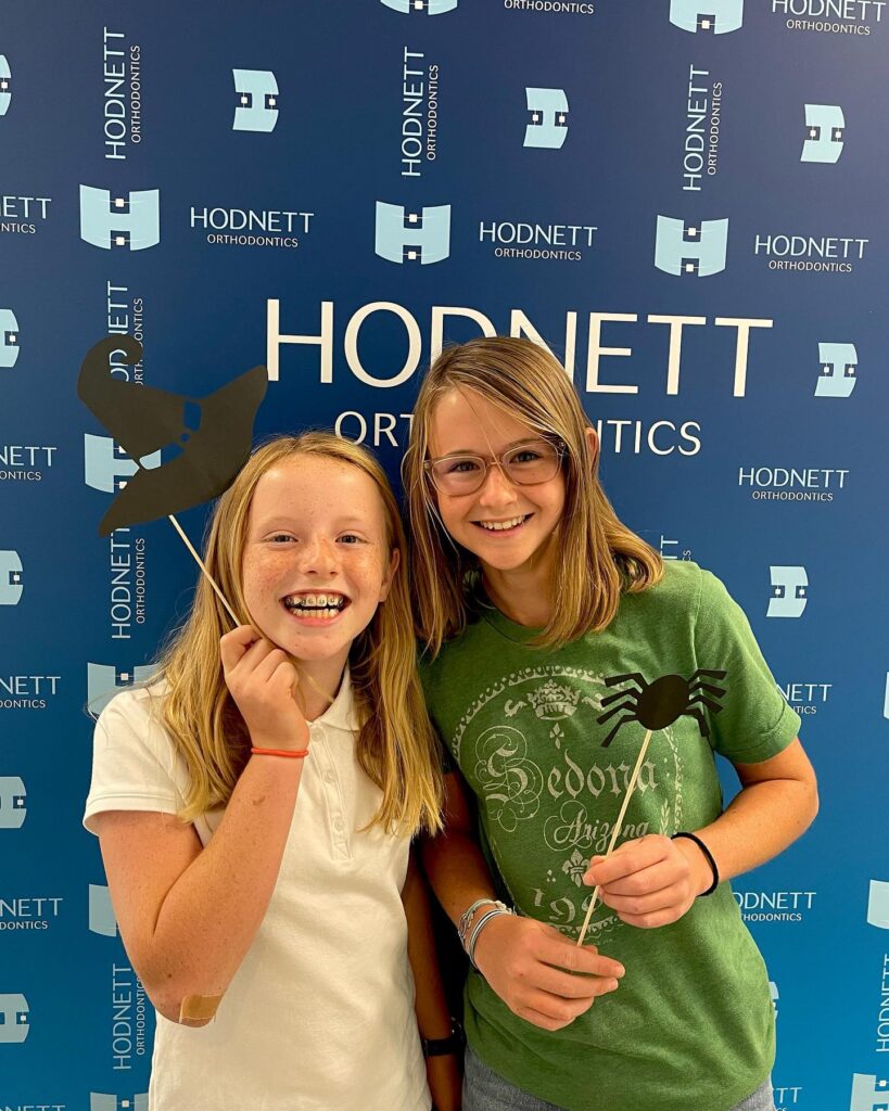 Two girls posing for a picture in front of a blue wall.